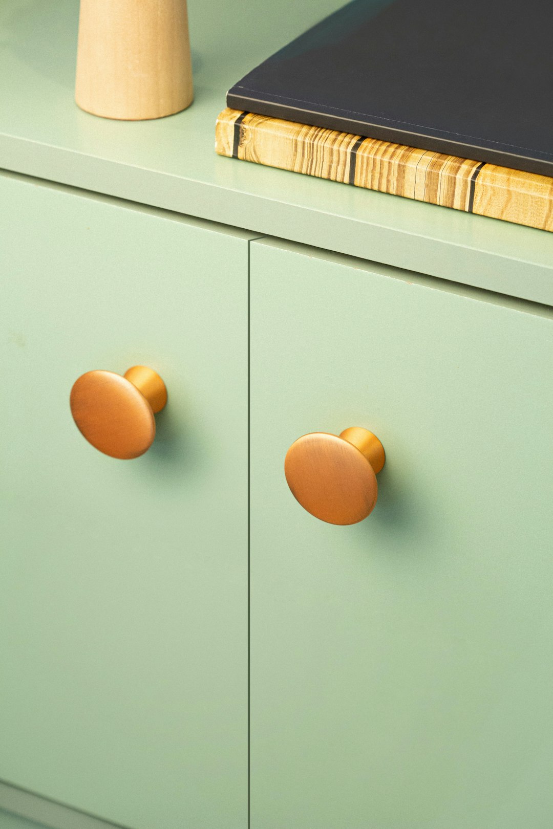 Cabinet in pastel green with round brushed bronze handles.